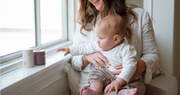 Mother holding her baby on her lap as the infant reaches for WeNatal for Her and Omega DHA+ supplement containers, highlighting essential prenatal nutrients for pregnancy and postpartum health.